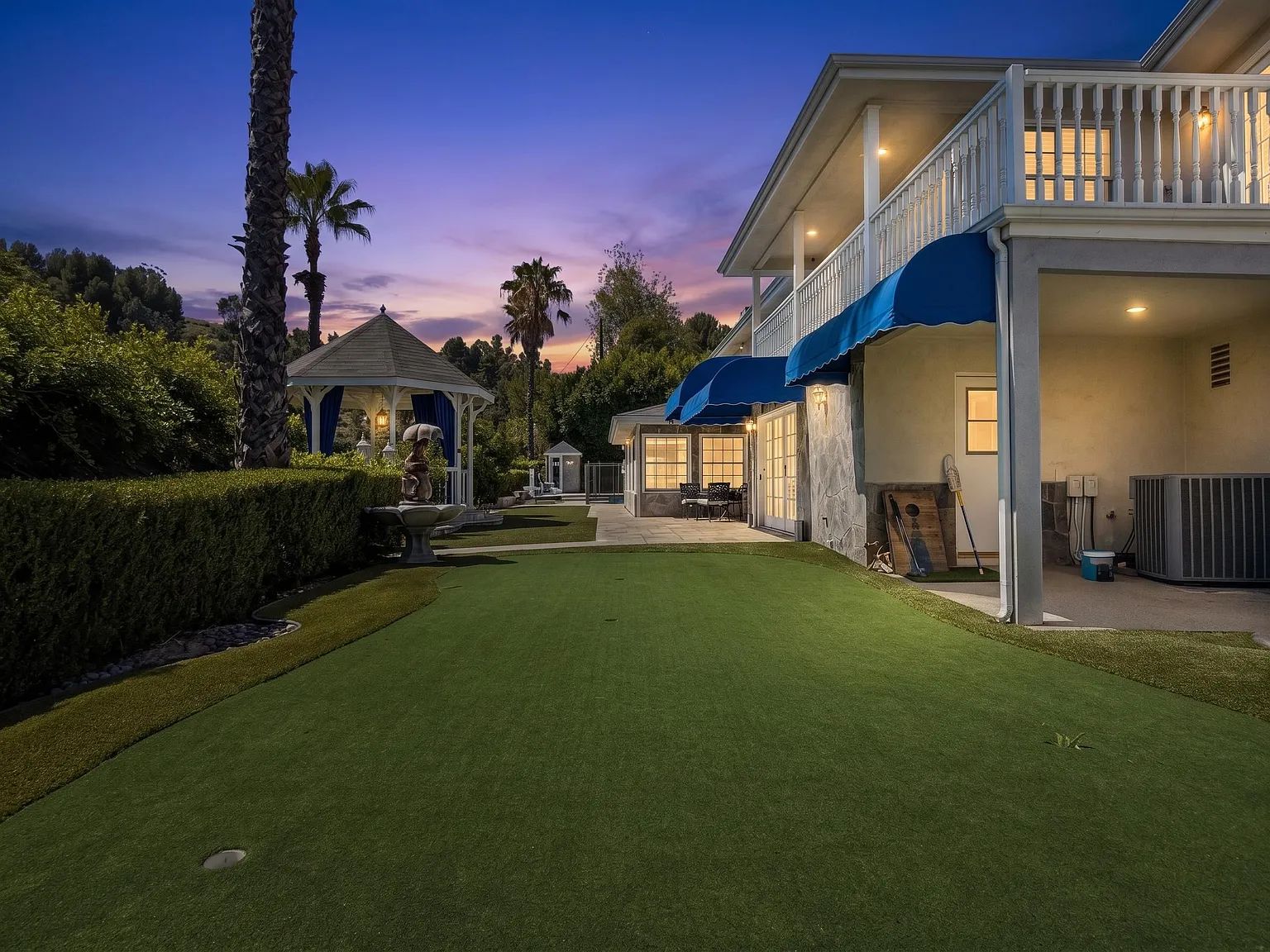 The backyard lawn at dusk with palm trees and string lights